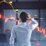 Man with a hand on his head looks at a red stock market chart showing a falling share price.