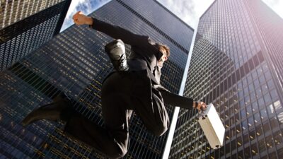 View from below of a banker jumping for joy in the CBD surrounded by high-rise office buildings.