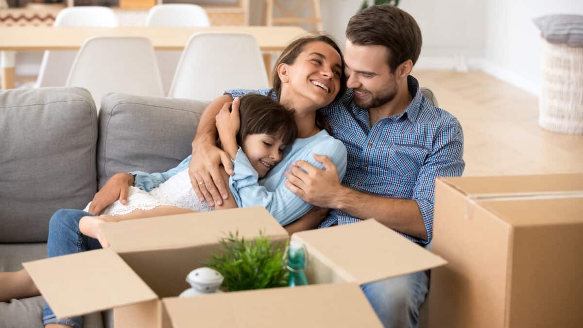 Happy mum and dad with daughter smiling on couch after relocation to new home.