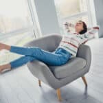 Woman relaxing at home on a chair with hands behind back and feet in the air.