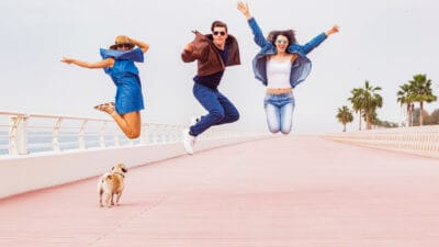 Three friends leaping in the air in joy with a dog on the ground.