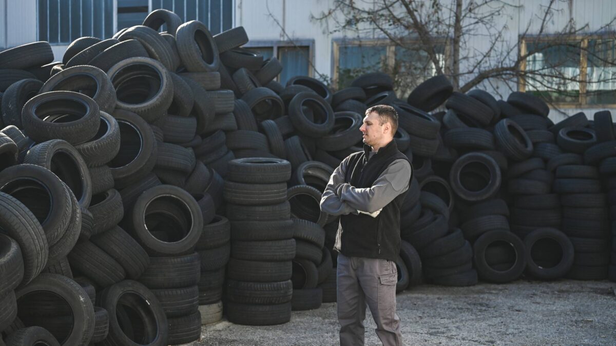 A man folds his arms as he stands amid a stack of used tyres.